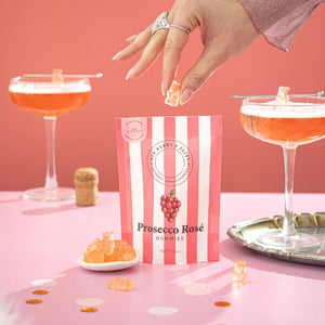 Prosecco Rosé gummies packaging with a hand reaching for a gummy, set against a pink background with cocktails.